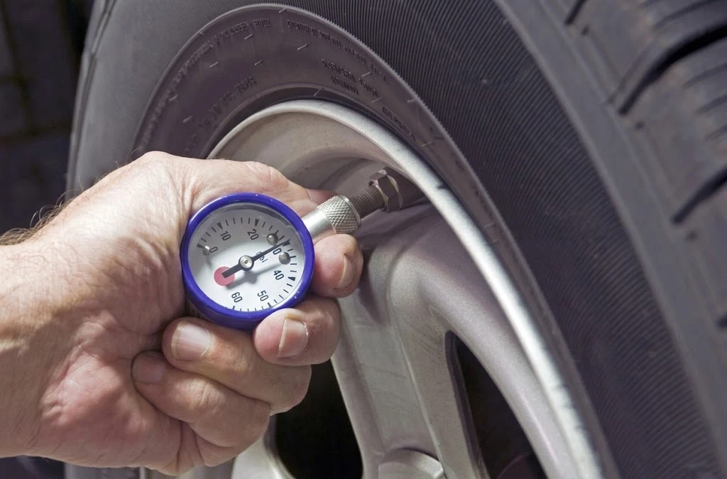 A person uses a professional pressure gauge to check a Kales Vehicle truck tire to prevent fuel economy penalties.